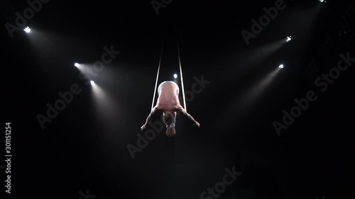 Muscular circus aerialist on the aerial straps in black studio photo