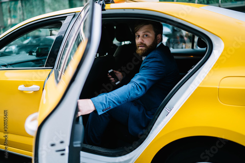 Fotografia, Obraz Portrait of handsome businessman looking at camera while sitting to cab for gett