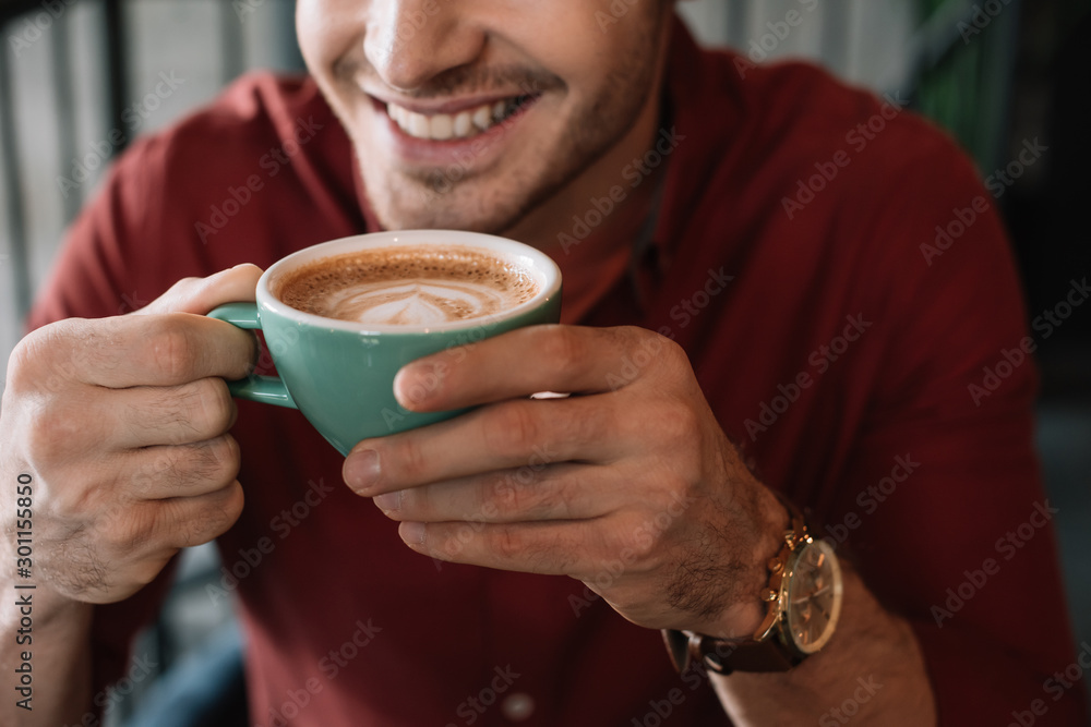 cropped view of smiling young man with cup of tasty cappuccino in coffee shop cropped view of smiling young man with cup of tasty cappuccino in coffee shop