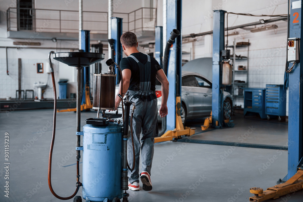 Big garage. Male mechanic use special device to repair broken automobile Big garage. Male mechanic use special device to repair broken automobile