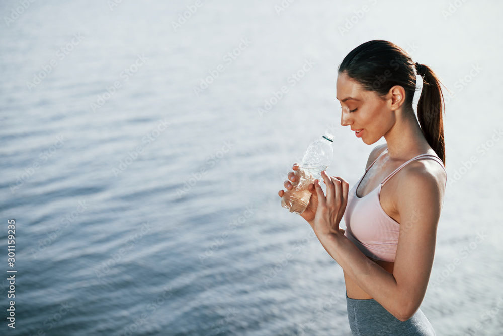 With bottle of water. Girl in sportive clothes stands against the lake With bottle of water. Girl in sportive clothes stands against the lake