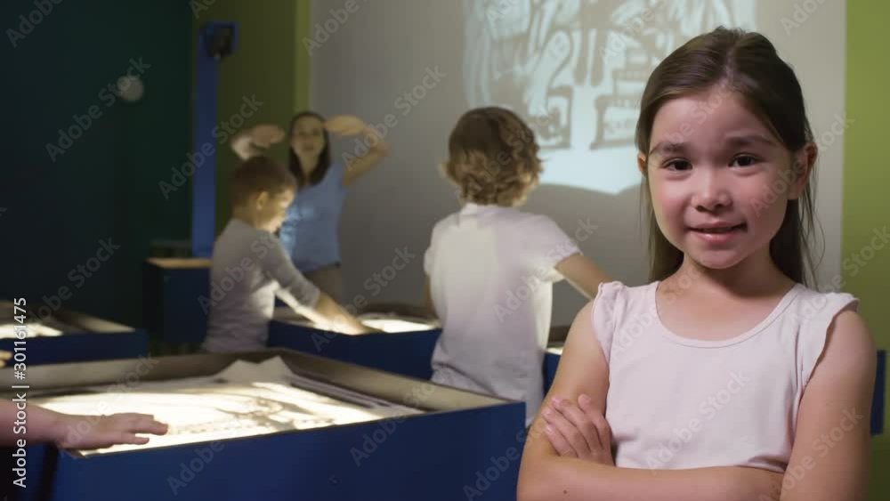 Medium shot of adorable little Asian girl standing with her arms crossed and smiling for camera in sand animation class Medium shot of adorable little Asian girl standing with her arms crossed and smiling for camera in sand animation class
