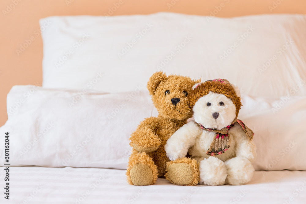 Cute little fluffy brown and white teddy bear on the bed with space on white pillow