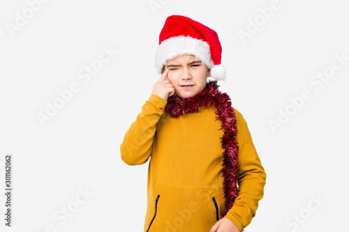 Little boy celebrating christmas day wearing a santa hat isolated showing a disappointment gesture with forefinger.