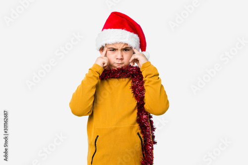 Little boy celebrating christmas day wearing a santa hat isolated focused on a task  keeping forefingers pointing head.