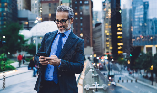 Mature satisfied male using mobile on urban background