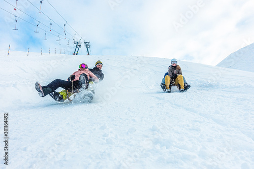 Tableau sur toile Crazy happy friends having fun with sledding on snow high mountains - Young mill