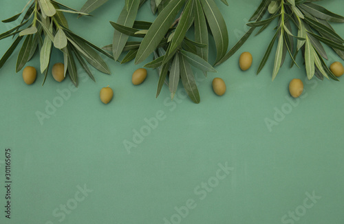 Flat lay Green Olives with olive branch with leaves on green background. Healthy food. Mediterranean diet. Poster, pattern, food background. With copy space for text or image. Top view.
