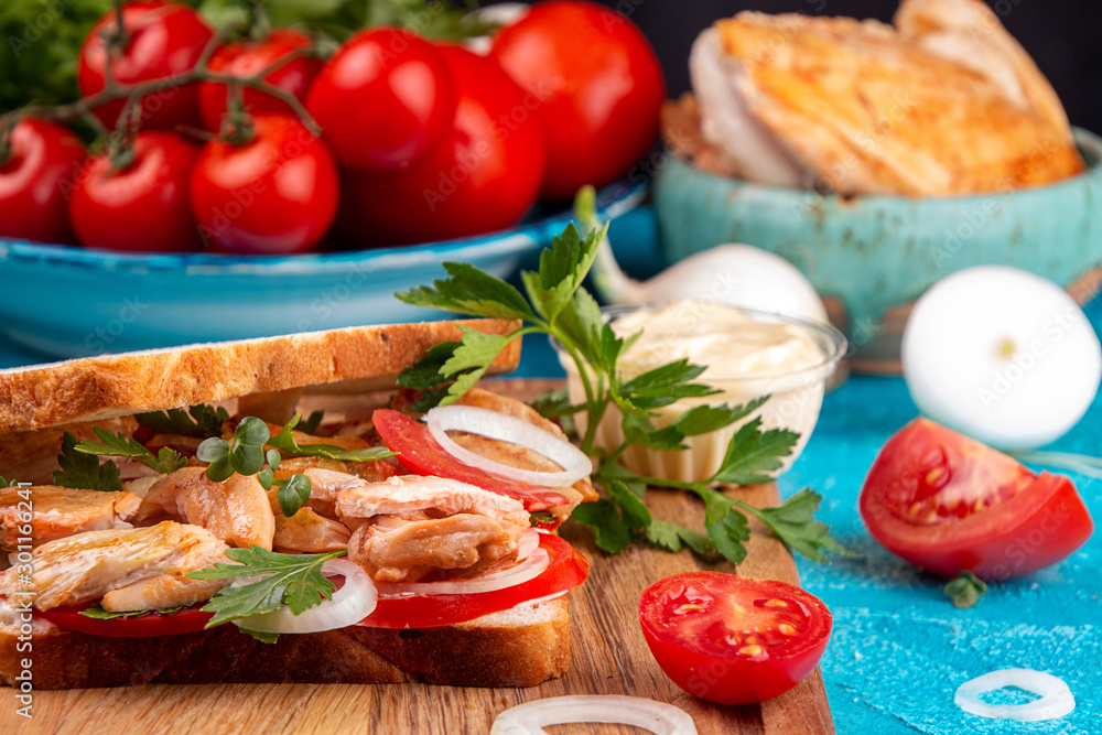 Sandwich with chicken meat, cherry tomato and onion on blue background