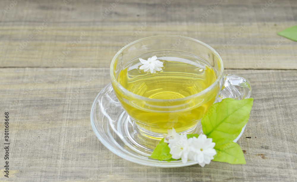 Glass cup with tea and fresh jasmine flowers on wooden table Glass cup with tea and fresh jasmine flowers on wooden table