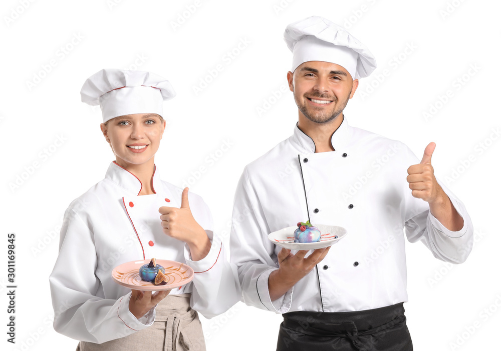 Young confectioners with tasty desserts showing thumb-up gesture on white background Young confectioners with tasty desserts showing thumb-up gesture on white background