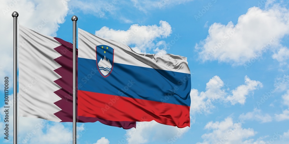 Qatar and Slovenia flag waving in the wind against white cloudy blue sky together. Diplomacy concept, international relations.