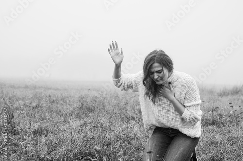 Fototapeta Girl closed her eyes on the knees, praying in a field during beautiful fog