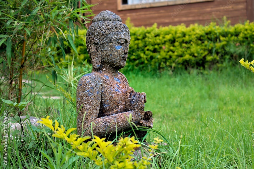 Cement made Buddha Statue among green grass and bamboo trees in garden Cement made Buddha Statue among green grass and bamboo trees in garden