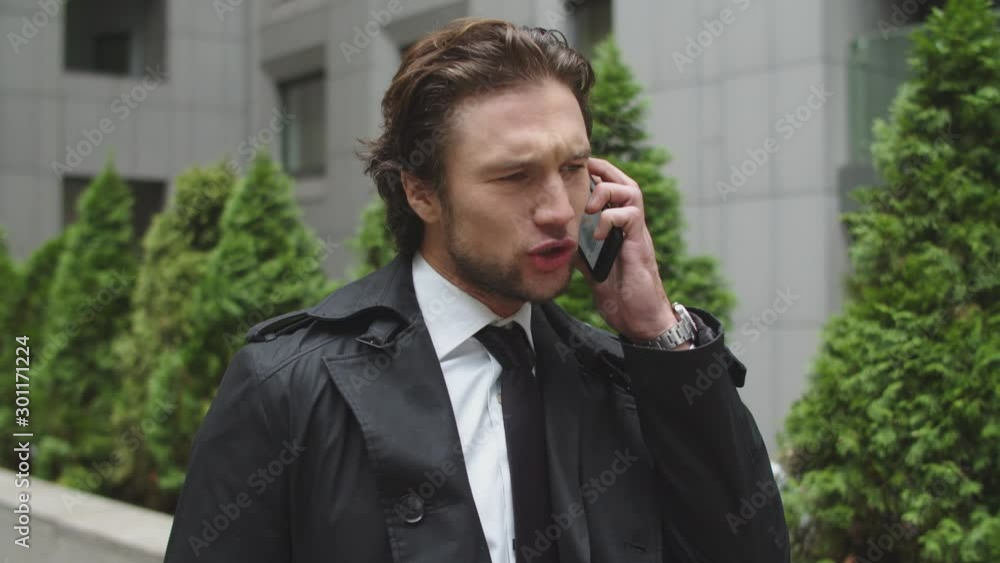 Young business man conducts tense telephone calls. He is upset and disappointed with the information received Young business man conducts tense telephone calls. He is upset and disappointed with the information received