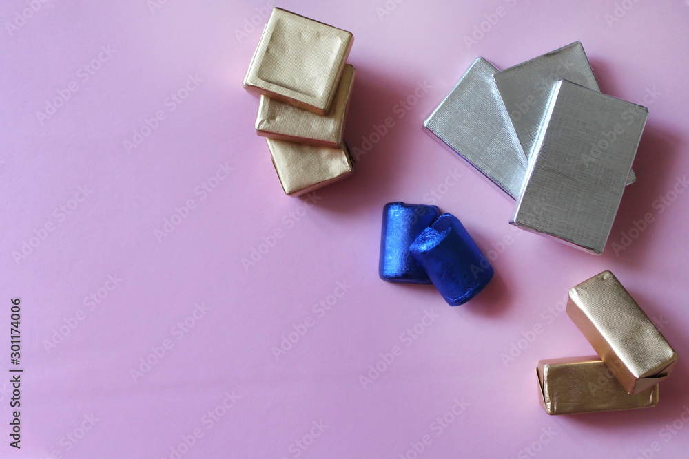 Pile of chocolates wrapped in silver, golden and blue foil. Copy space for text. Template for greeting card, poster or invitation. Sweet candies on pink smooth table. Backdrop or background Pile of chocolates wrapped in silver, golden and blue foil. Copy space for text. Template for greeting card, poster or invitation. Sweet candies on pink smooth table. Backdrop or background