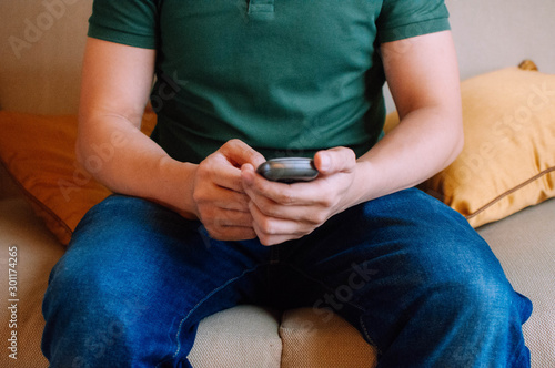 A young male adult is using a device to measure blood sugar while sitting on a couch © mrkarlph