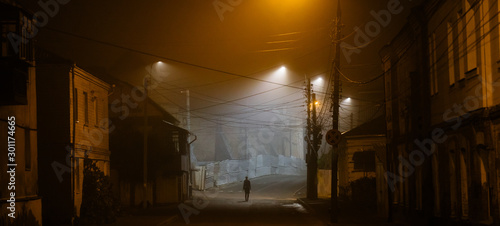 Lonely woman walking in foggy old city with street lights in a coat photo