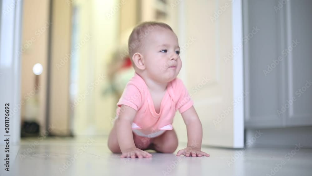 A little one year old infant baby girl in a pink bodysuit crawls on the floor. A little one year old infant baby girl in a pink bodysuit crawls on the floor.