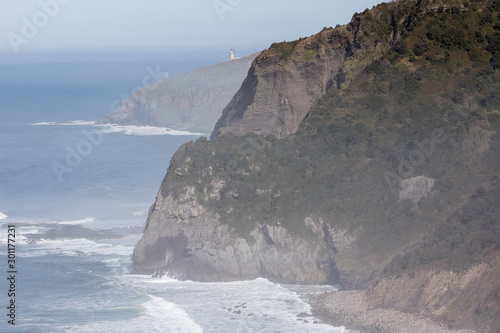 View down the misty Basque coastline towards a lighthouse from San Juan de Gaztelugatxe, Spain 