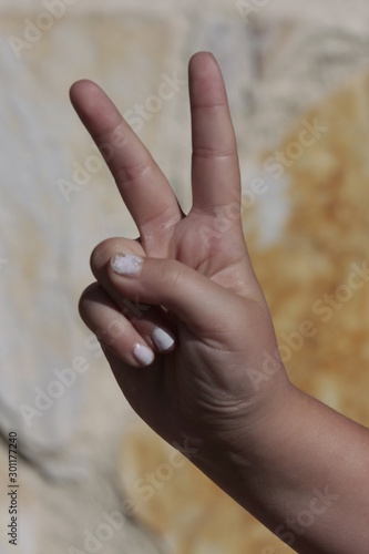Mano de niña con las uñas pintadas de blanco realizando distintos signos.