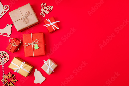 Photo of creative conept of presents wrapped among new year items like bells skates and snowflakes near copyspace isolated vibrant color red background © deagreez