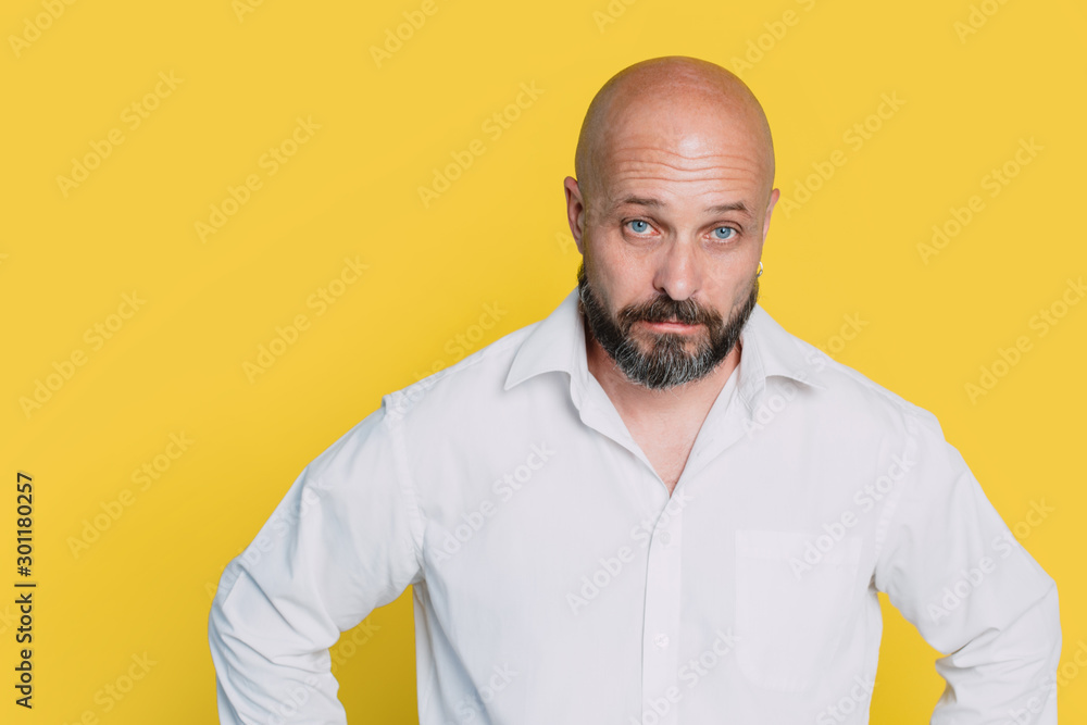 Serious middle-aged man with folded arms and a deadpan expression posing in front of a yellow background with copy space Serious middle-aged man with folded arms and a deadpan expression posing in front of a yellow background with copy space