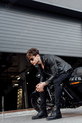 full length view of handsome man sitting on motorcycle with clenched hands and looking forward