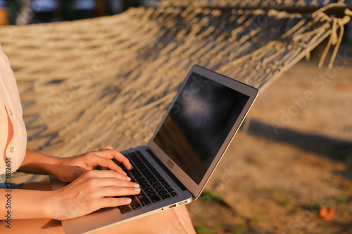 Close up caucasian female person using laptop and sitting on wicker hammock. photo