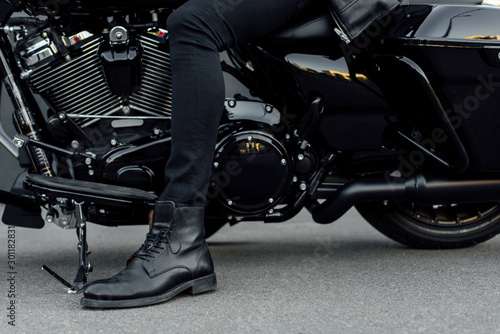 cropped view of man in black boot sitting on motorcycle