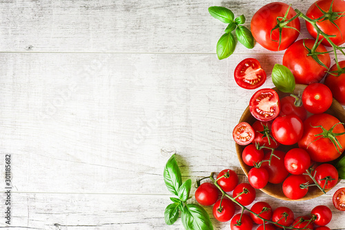 Fresh tomatoes in bowl on rustic white table top view. Tomato red background healthy food vegetables and ripe basil leaves on old board.