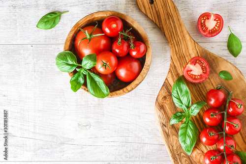 Fresh tomatoes and basil on cut board white table  top view. Beautiful red tomato vegetables concept with copy space.