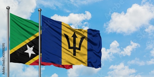 Saint Kitts And Nevis and Barbados flag waving in the wind against white cloudy blue sky together. Diplomacy concept, international relations.