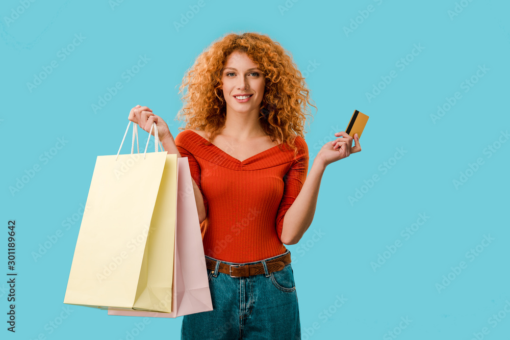smiling woman holding shopping bags and credit card, Isolated On blue - obrazy, fototapety, plakaty 