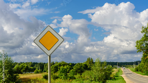 Priority road sign near asphalt road on the background of dramatic clouds and blue sky photo