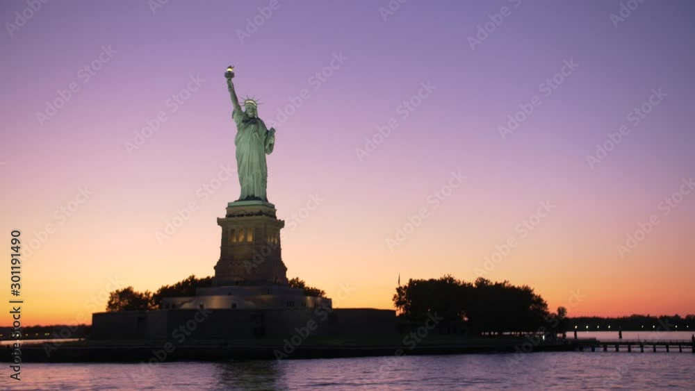 establishing shot of Statue of liberty silouhette at dawn, shot from a boat on orange and violet sky establishing shot of Statue of liberty silouhette at dawn, shot from a boat on orange and violet sky