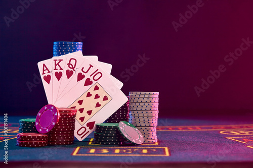 Winning combination in poker standing leaning on multicolored chips piles on blue cover of playing table. Black background. Casino concept. Close-up.