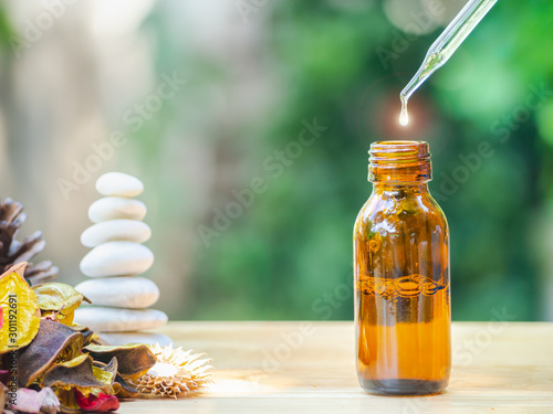 The essential oil falling from glass dropper into organic bio alternative medicine, brown bottle.