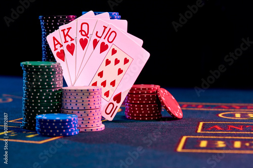 Winning combination in poker standing leaning on multicolored chips piles on blue cover of playing table. Black background. Casino concept. Close-up.