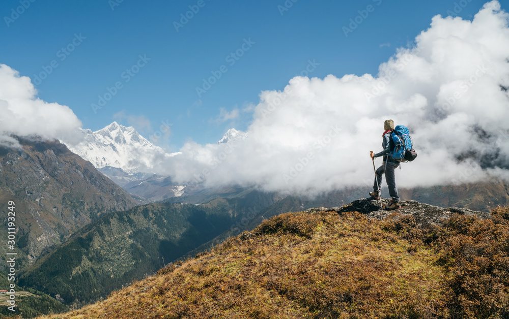 Young hiker backpacker man using trekking poles enjoying the Nuptse 7861m mountain during high altitude Acclimatization walk. Everest Base Camp trekking route, Nepal. Active vacations concept image