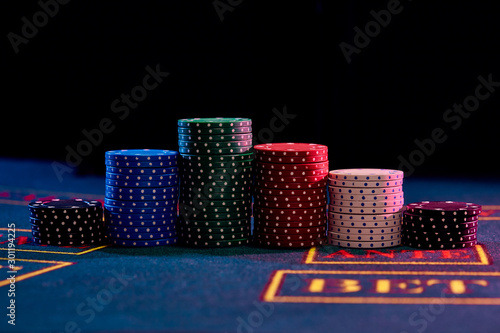 Colorful chips piles standing on blue cover of playing table. Black background. Gambling entertainment, poker, casino concept. Close-up.