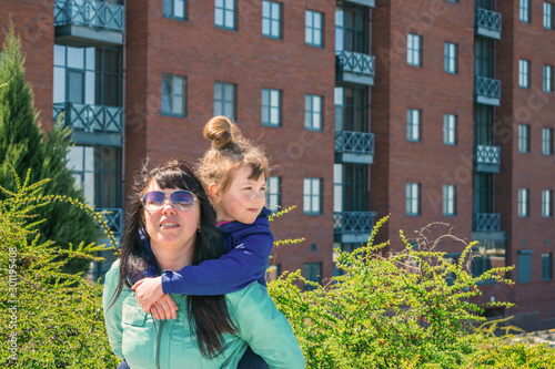 Mom hugs with her daughter on the background of a country house. A woman and a child are happy to move to a new apartment. The family is near the apartment building.
