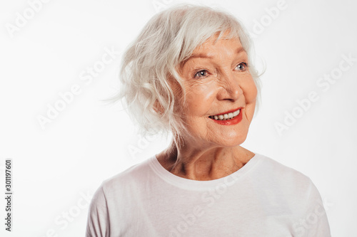 Portrait of happy, cheerful and positive old woman posing on camera alone. Amazing and beautiful smile. Close up. Wear white shirt. Stand alone. Isolated over white background.