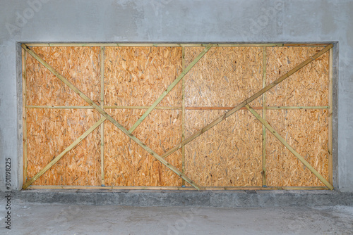 A large entrance to the garage secured with OSB boards, which are nailed with strips from the inside.