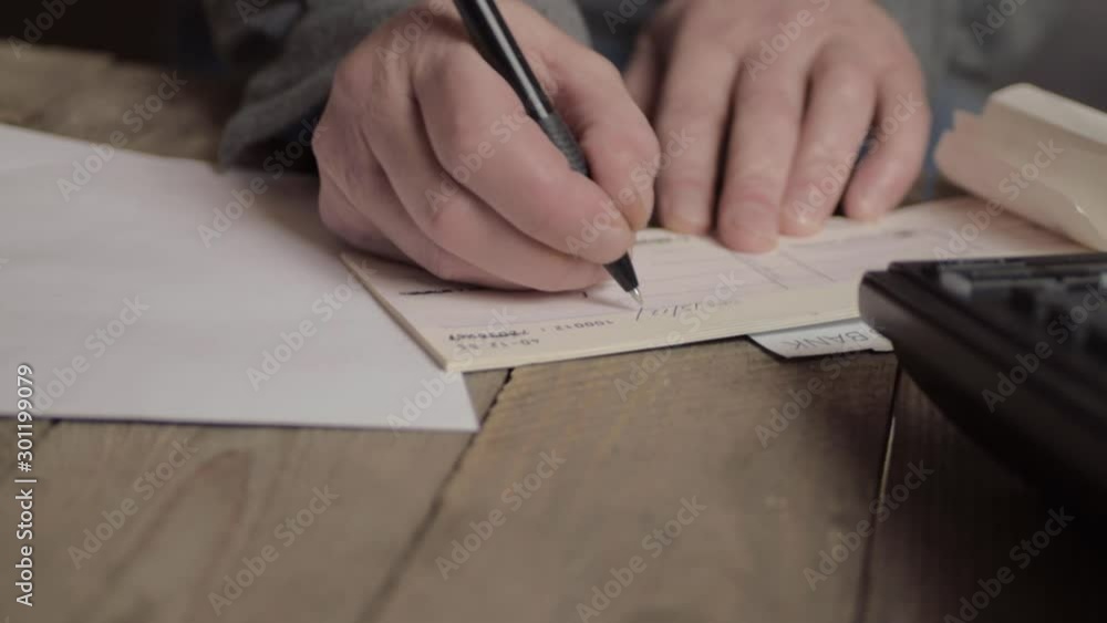Hand of busy person writing a banking check to pay bills in office with phone