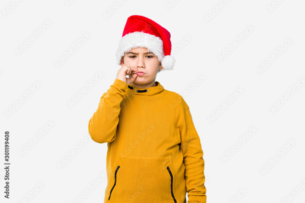 Little boy celebrating christmas day wearing a santa hat isolated with fingers on lips keeping a secret. Little boy celebrating christmas day wearing a santa hat isolated with fingers on lips keeping a secret.