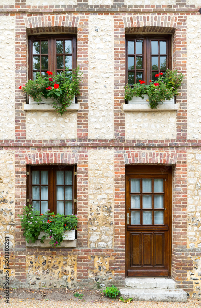 typical Normandy architecture house front with stone and brick facade and colorful flowerpots