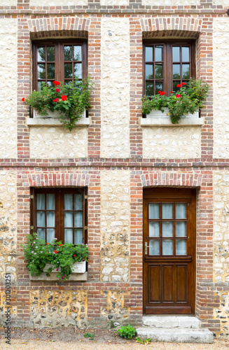 typical Normandy architecture house front with stone and brick facade and colorful flowerpots