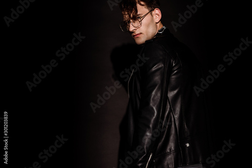 trendy man in glasses and leather jacket standing on black