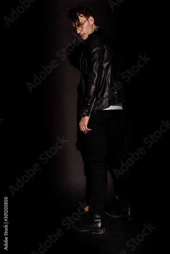 stylish man in glasses and leather jacket standing on black